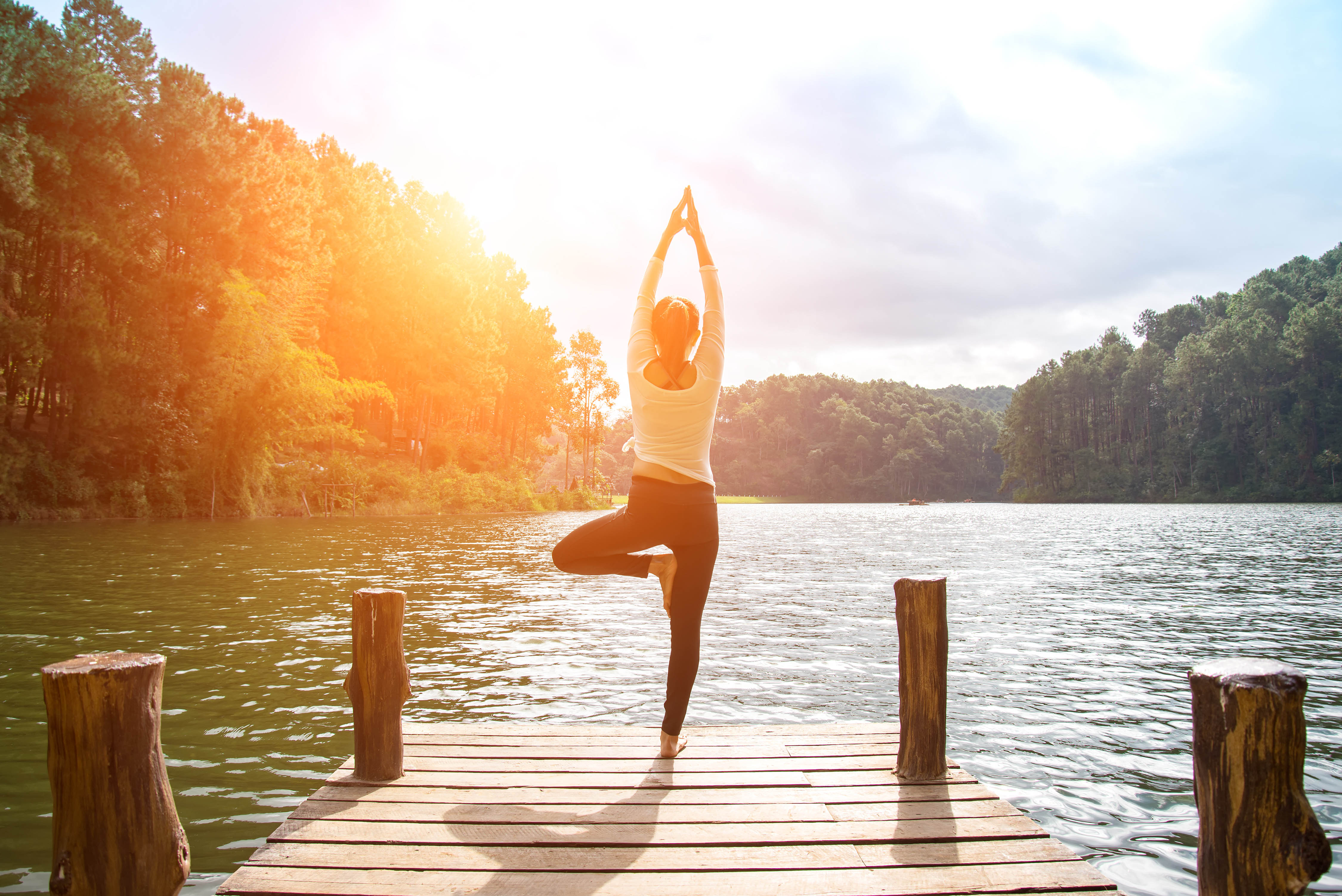 Back of a woman on a dock, at the water's edge, doing yoga as the sun sets Back of a woman on a dock, at the water's edge, doing yoga as the sun sets